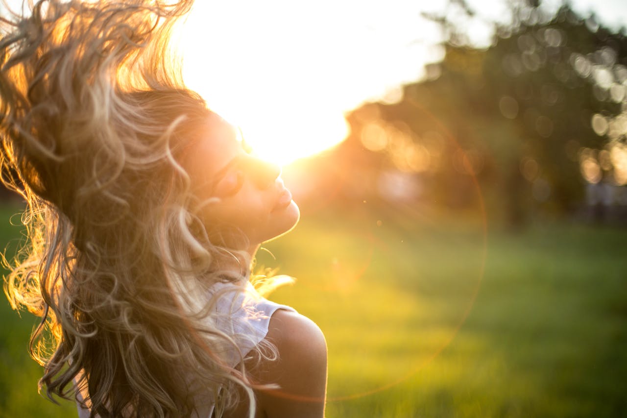 A young woman tosses her long, wavy blond hair in the sunlight during golden hour outdoors.